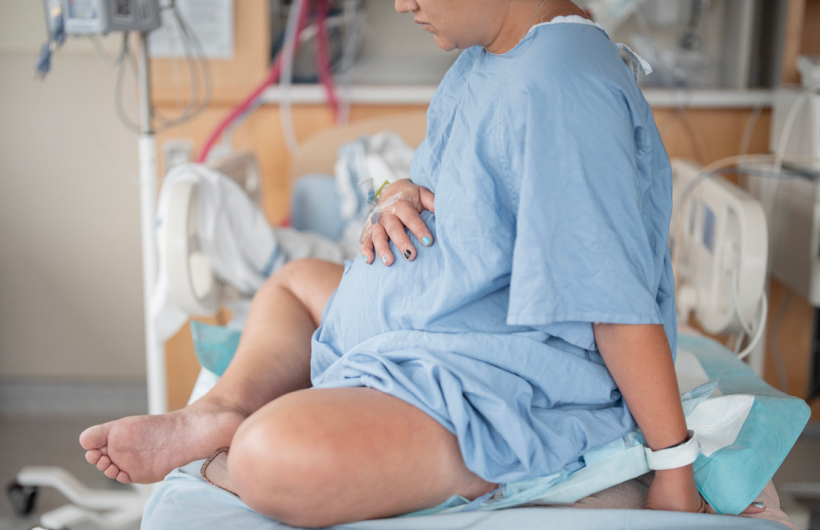 A pregnant woman in a blue hospital gown sits in a hospital bed, waiting to give birth